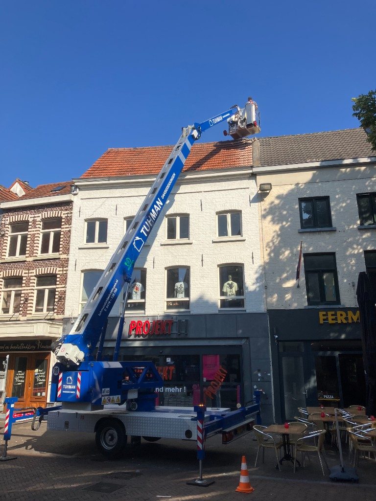 Hoogwerker van Tuhman aan het werk op een pannendak in een winkelstraat
